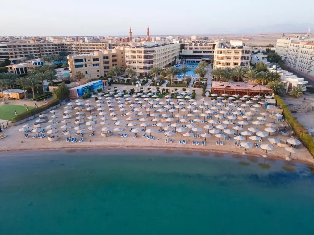 Плажът с чадъри от палмови листа и хотелът зад него – AMC Royal Hotel & Spa, Хургада