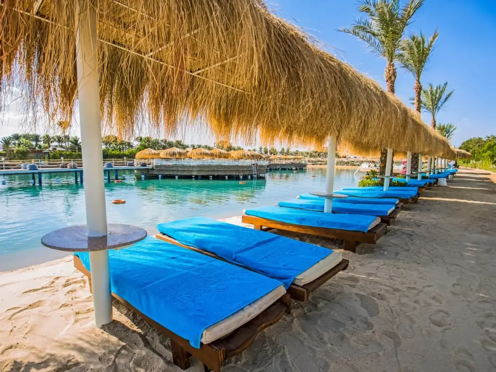 Шезлонги със сини дюшеци под сламен чадър на пясъчния плаж – Sunrise Aqua Joy Resort, Хургада
