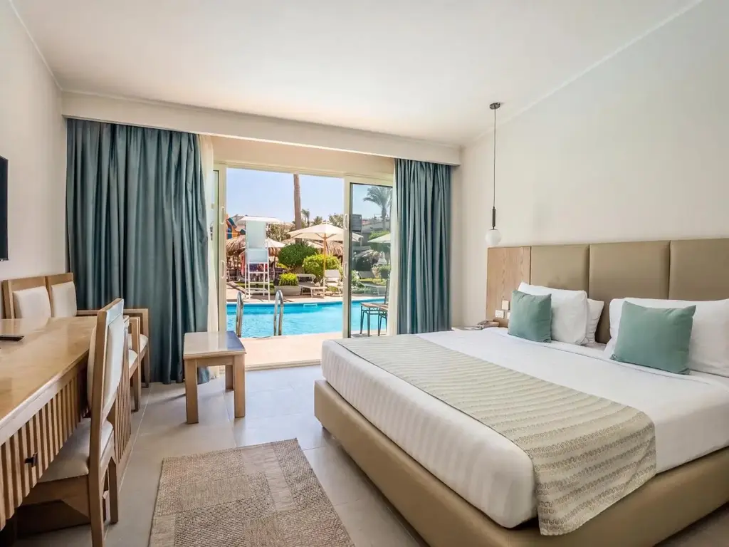 Двойно легло, бюро и стъклена врата към басейна сред палмите – Sunrise Aqua Joy Resort, Хургада